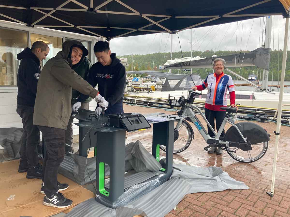 Installation of the first of seven e-bike charging stations on the Island - at the Gore Bay Marina - is overseen by MICA’s president, Maja Mielonen, on an e-bike. Photo by Isobel Harry.